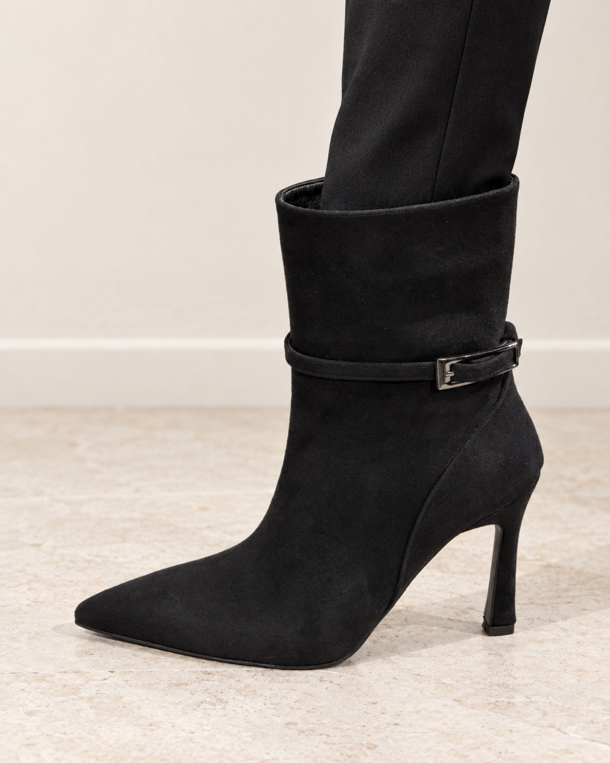 Vivienne Suede Buckle Ankle Boot in black by VIVACE, worn with slim black trousers on a pale stone floor.