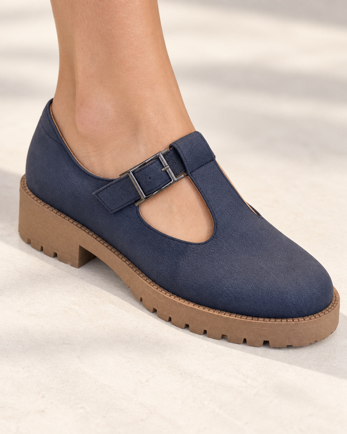 A single foot wearing the VIVACE Marielle navy T-bar shoe with a dark buckle and tan lug sole on a light neutral floor.